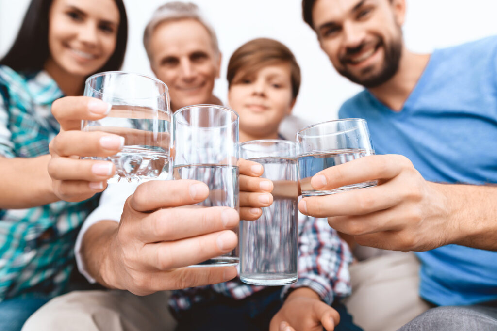 Eine glückliche, generationenübergreifende Familie stößt mit Gläsern voller klarem, gefiltertem Wasser an.
