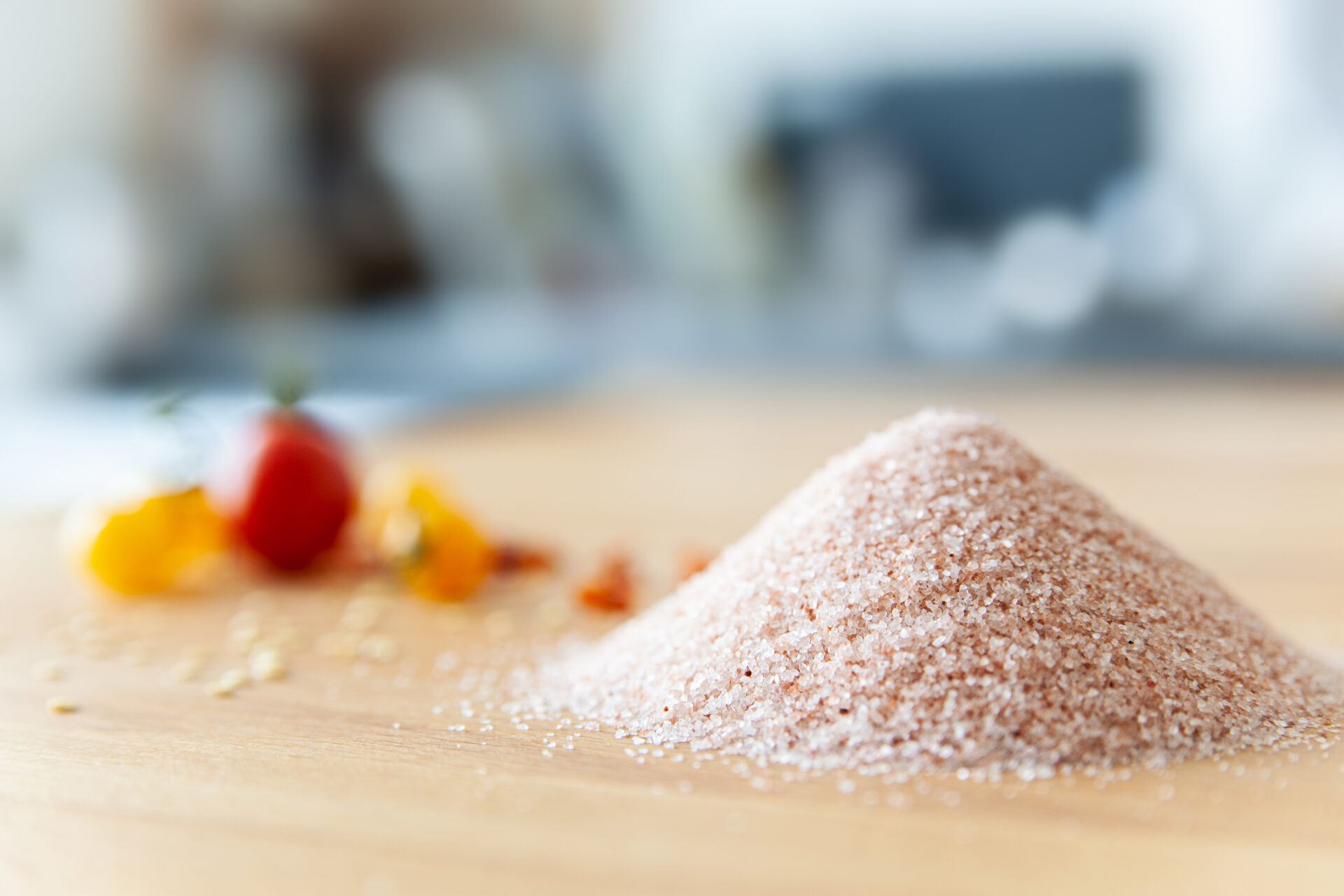 Ein Haufen feines rosa Kristallsalz liegt auf einem Holzbrett, mit bunten Tomaten im Hintergrund.