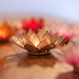 Ein Teelichthalter in Form einer goldenen Lotusblüte mit brennender Kerze schafft eine warme, gemütliche Atmosphäre auf einem Holztisch.