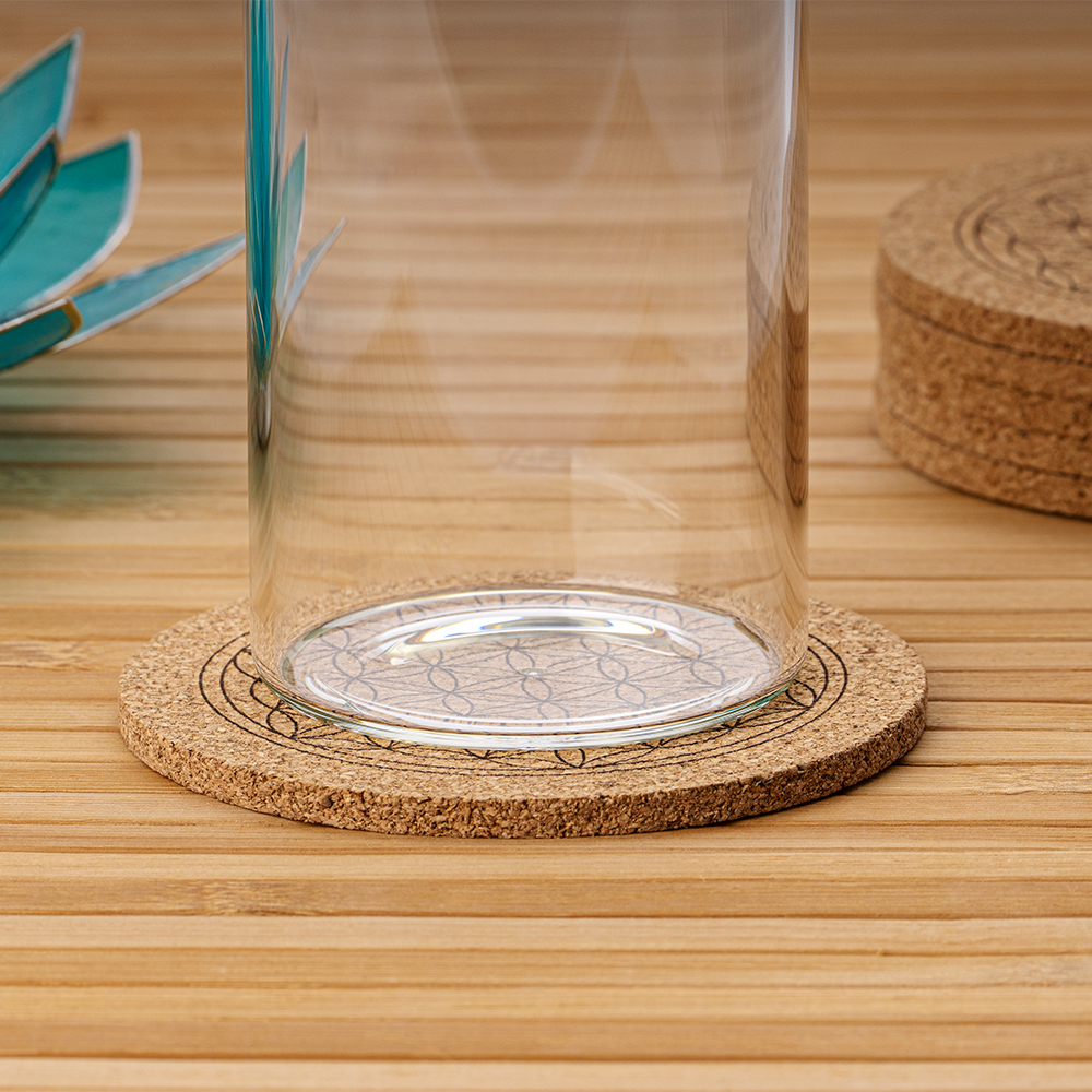 Eine Glaskaraffe steht auf einem runden Korkuntersetzer, der mit dem Symbol der Blume des Lebens graviert ist und auf einem Holztisch liegt.