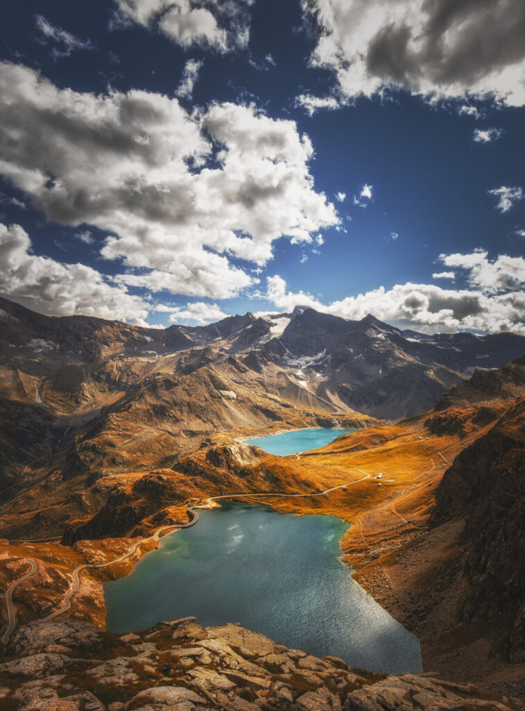 Zwei unberührte, leuchtend blaue Bergseen in einer weiten alpinen Landschaft unter einem Himmel mit dramatischen Wolken.