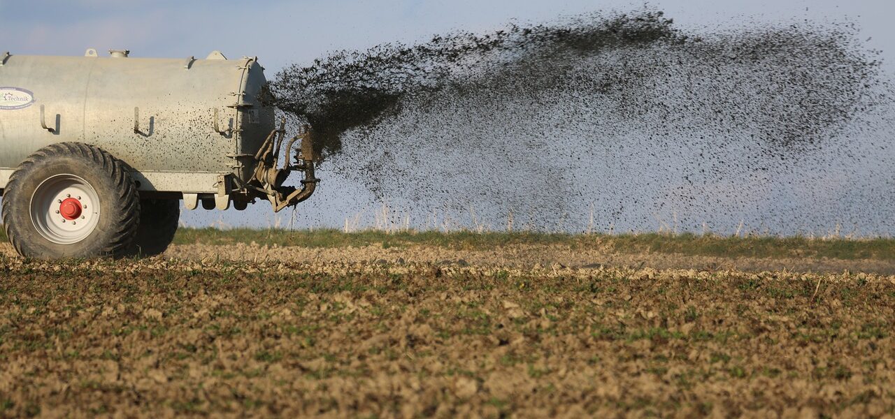Landwirtschaftsfahrzeug fährt über Feld und versprüht Dünger - ein Grund für Nitrat im Trinkwasser.