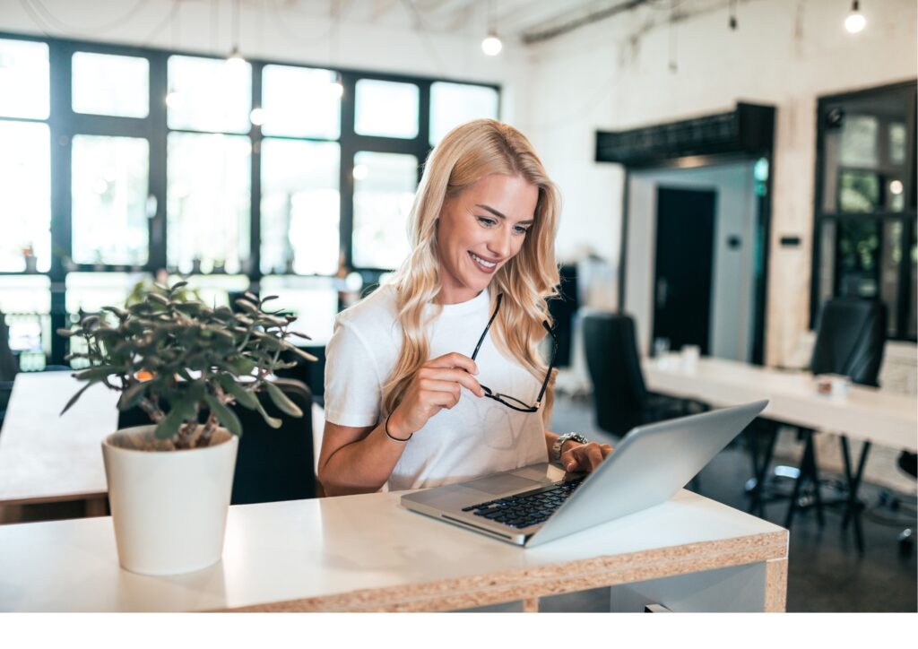 Eine Frau sitzt lächelnd vor ihrem Laptop und nimmt am Lotus Vita Empfehlungsprogramm teil.