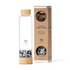 Eine wiederverwendbare Glas-Trinkflasche mit Bambusdeckel und einem separaten Fach gefüllt mit schwarz-weißen Kristallsteinen, stehend neben der Produktverpackung.
